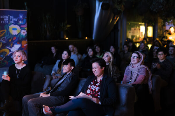 Photo of Attendees at the Liminal emerging writers festival - they look like they are watching something on stage and are bathed in stage light in an intimate and relaxed setting.